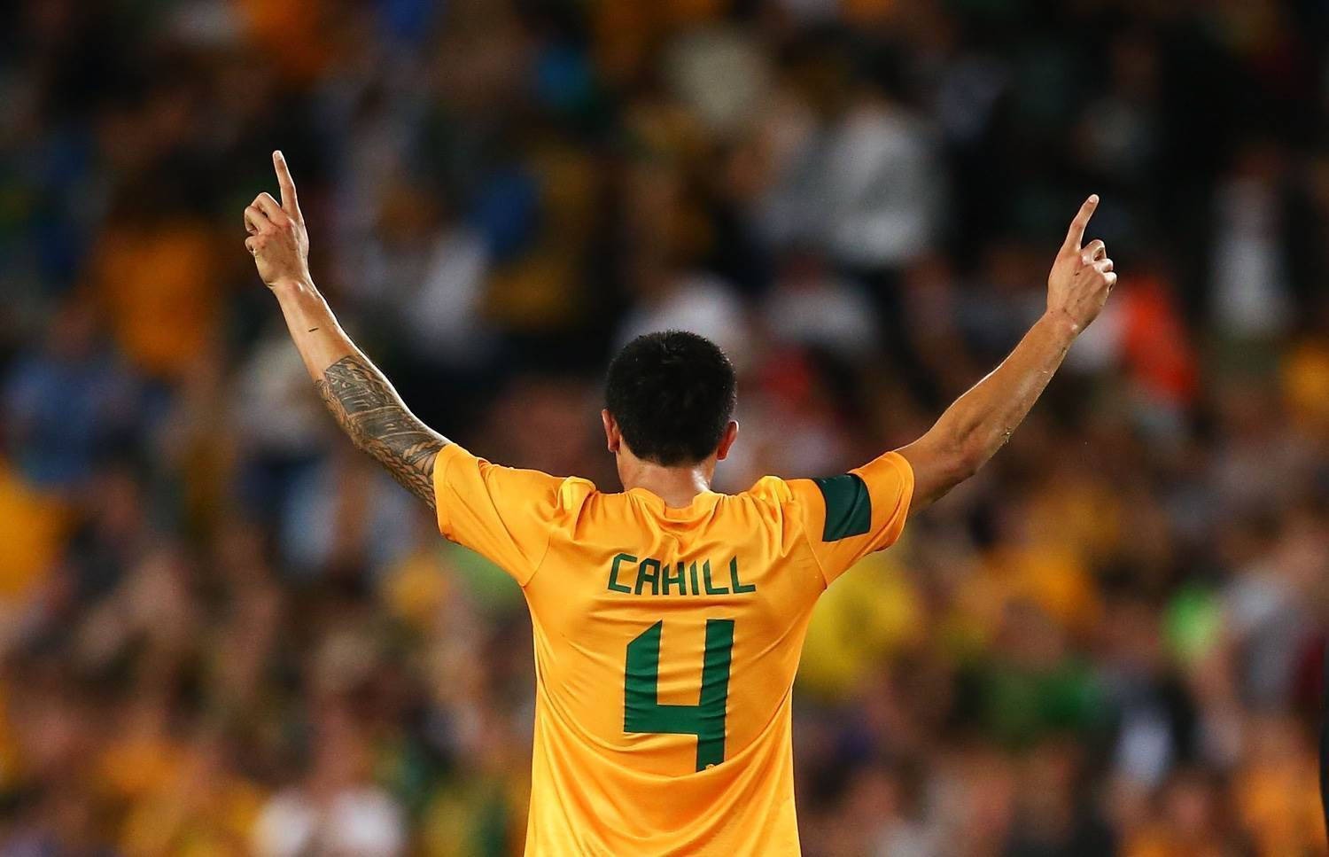 Jogador da seleção australiana de costas usando camisa amarela com detalhes verdes durante partida de futebol.
