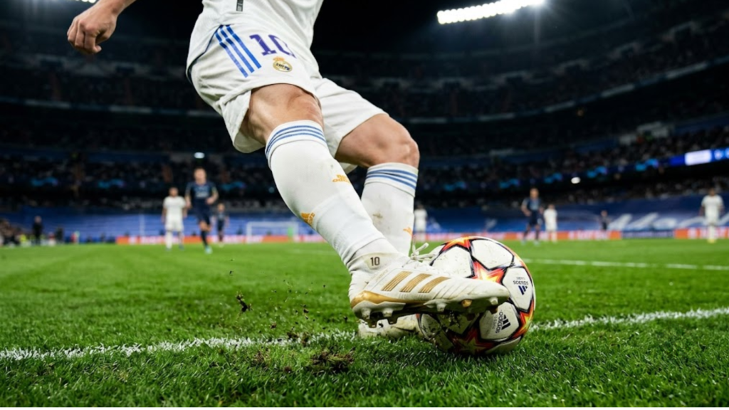 Close no pé de Luka Modric executando um passe milimétrico com a parte externa da chuteira em um gramado à noite sob as luzes do estádio.