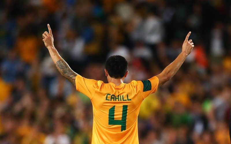 Jogador da seleção australiana de costas usando camisa amarela com detalhes verdes durante partida de futebol.